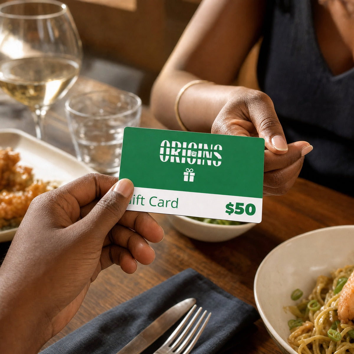 Origins fifty dollar gift card exchanged between two people across a restaurant table.