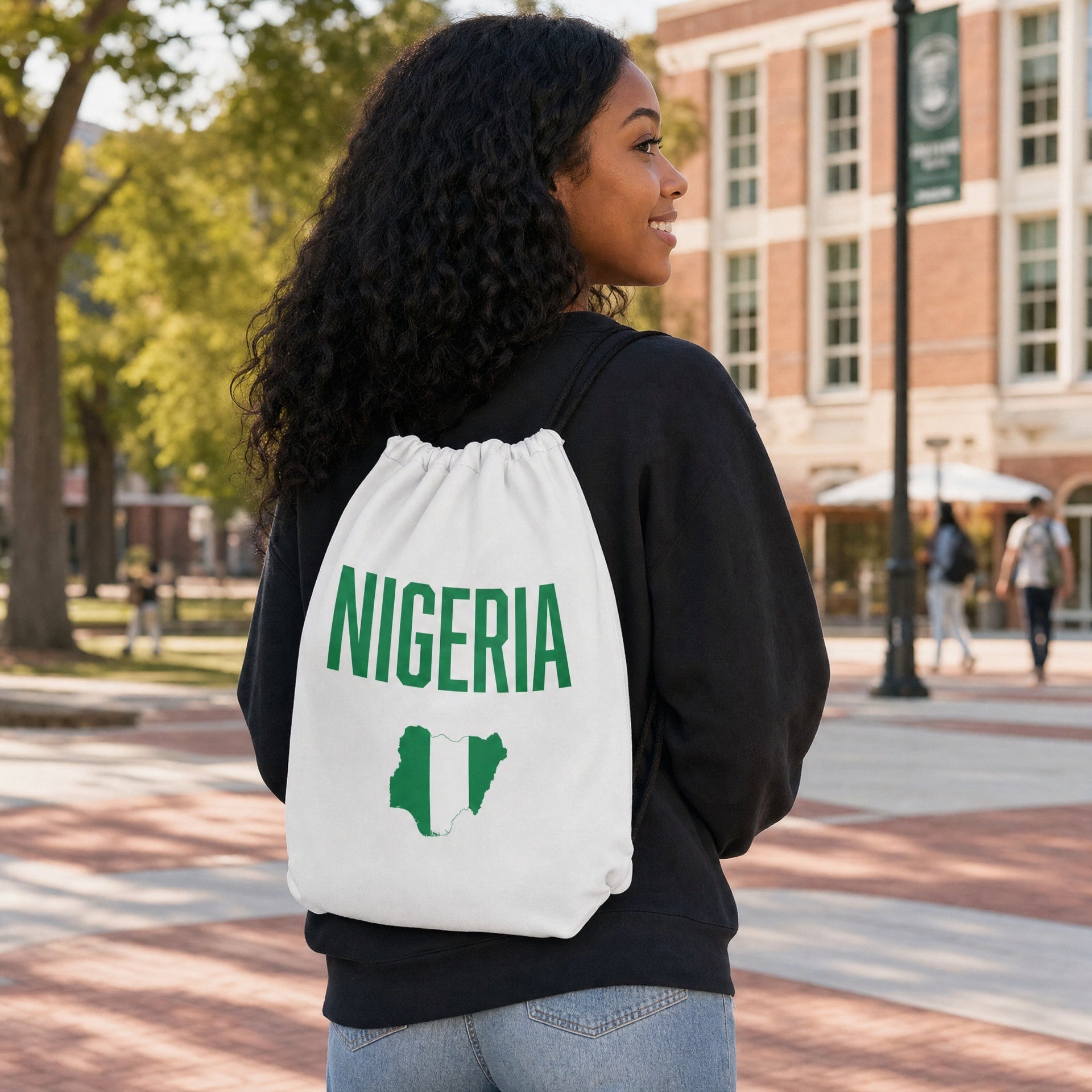 Woman wearing the white Nigeria Classic drawstring bag with green Nigeria map graphic on a campus walkway.