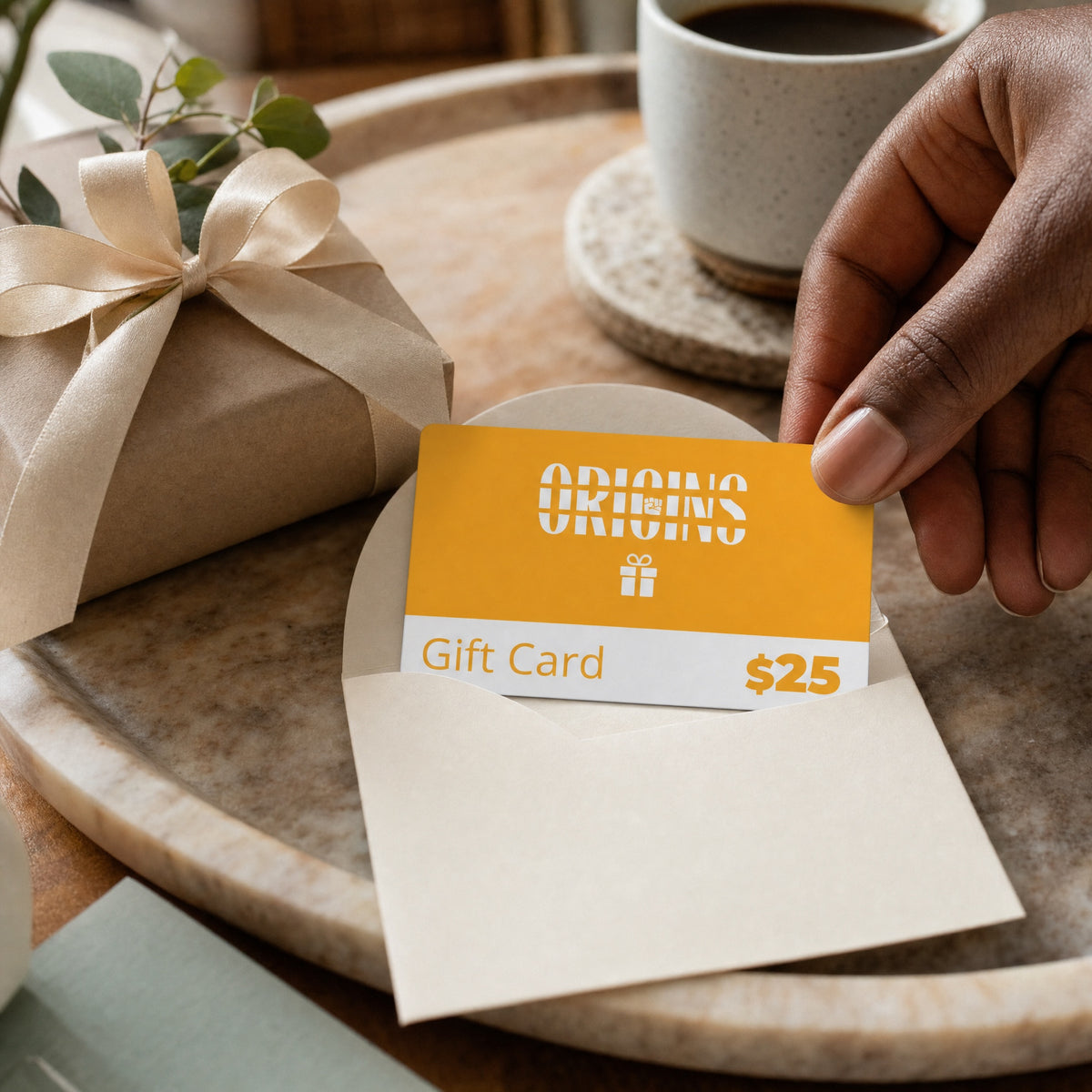 Origins twenty-five dollar gift card beside a wrapped gift and envelope on a coffee table.